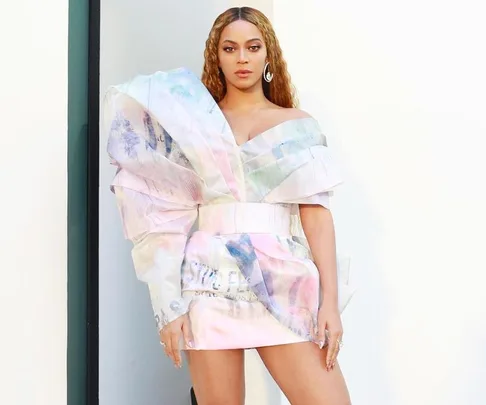 Beyoncé in a pastel abstract-patterned dress with ruffled sleeves, standing against a light background.