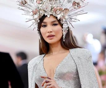 A woman in a silver dress with a jeweled headpiece at a formal event.