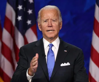 A man in a suit speaks at a podium with U.S. flags in the background.