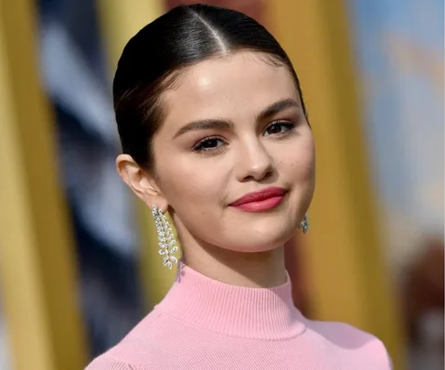 Young woman with dark hair in a sleek bun, wearing a pink top and sparkling earrings, smiling slightly.