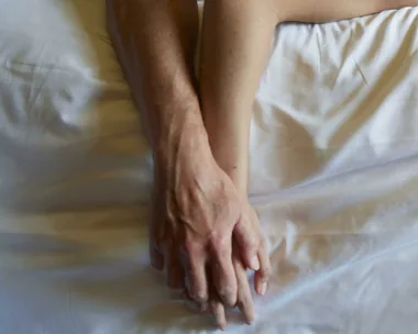 Two hands gently clasped on a white bedsheet, symbolizing intimacy and connection.