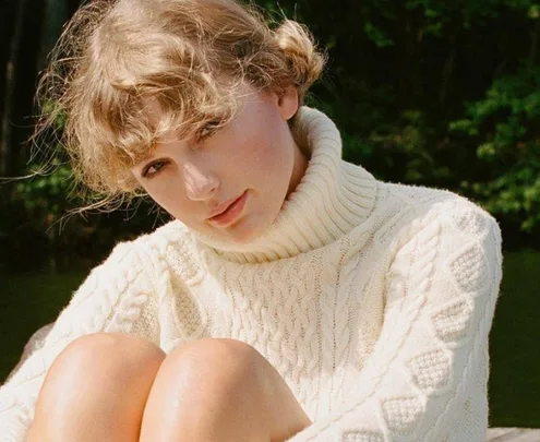 A person wearing a cozy cream cable-knit sweater, sitting outside with a soft expression, surrounded by greenery.