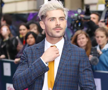 Man with blonde hair and plaid suit adjusting tie at a public event.