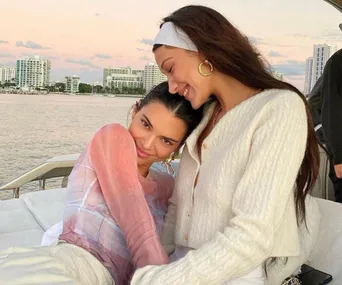 Two women smiling and embracing on a yacht with a city skyline and sunset in the background.