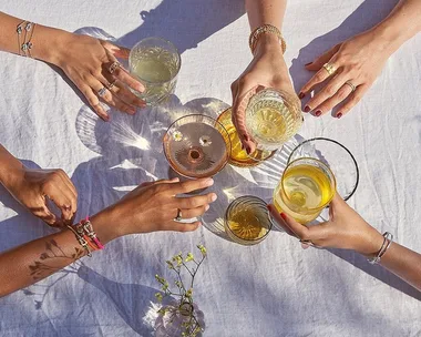 Hands adorned with Fred jewelry holding drinks over a white tablecloth.