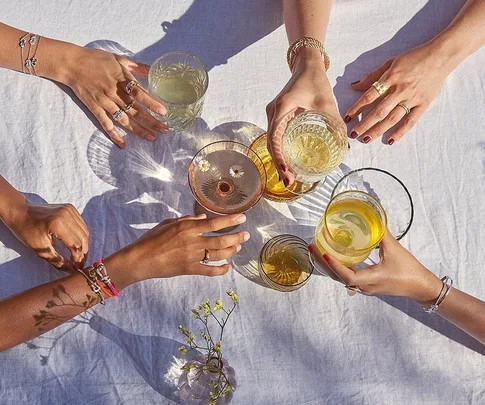 Hands adorned with Fred jewelry holding drinks over a white tablecloth.