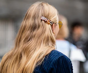 Woman with long blonde hair wearing a Gucci barrette and blue top, seen from behind.