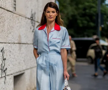 Person in light blue and red-trimmed pajamas stands outside, holding a bag.