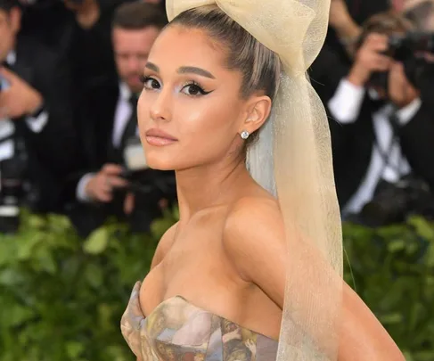 A woman in a strapless gown with a large hair bow at a formal event, surrounded by photographers.