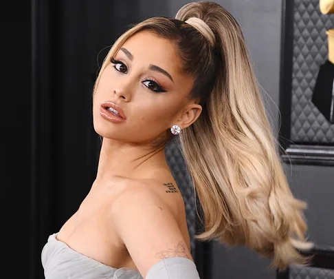 A woman with long, high ponytail and diamond earrings poses elegantly at an indoor event.