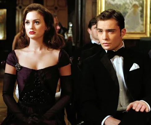 A woman in a dark elegant dress and a man in a tuxedo sit side-by-side at a formal event.