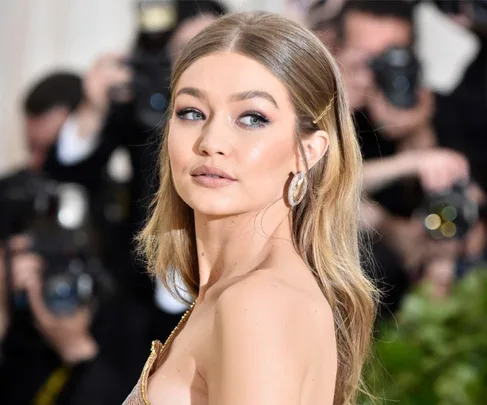 A person with long, styled hair and earrings poses confidently in front of photographers.