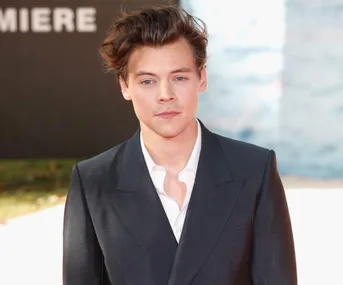 Young man with styled hair wearing a dark suit with white shirt, standing outdoors during daytime.