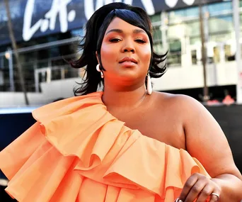 Person in an orange ruffled dress poses confidently outside, with an "L.A." sign blurred in the background.