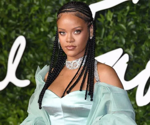 A woman in a mint green dress with braided hair at an event, wearing a diamond necklace and earrings.