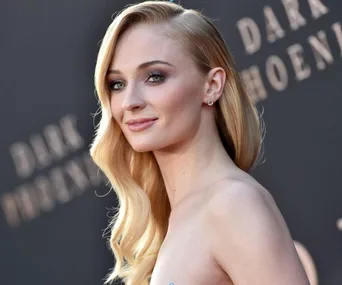 Blonde woman smiling at a movie premiere event with "Dark Phoenix" visible in the background.