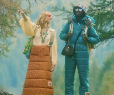 Two models in colorful retro outdoor wear from The North Face x Gucci collection standing amidst lush greenery.