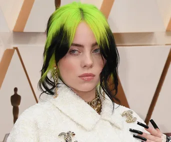 Billie Eilish with neon green and black hair, wearing a white outfit with Chanel logo, at an event.