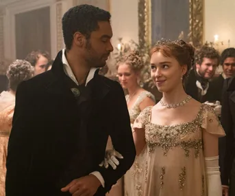 A couple in Regency-era attire dances at a formal ball, with decorative flowers and mirrors in the background.