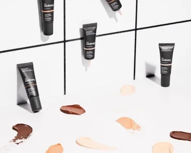 The Ordinary concealers on a white tiled surface with various shade swatches spread out.