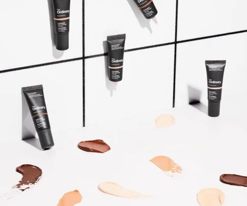 The Ordinary concealers on a white tiled surface with various shade swatches spread out.