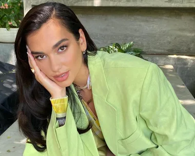 Person in a light green jacket leaning on a stone ledge, with lush greenery in the background.