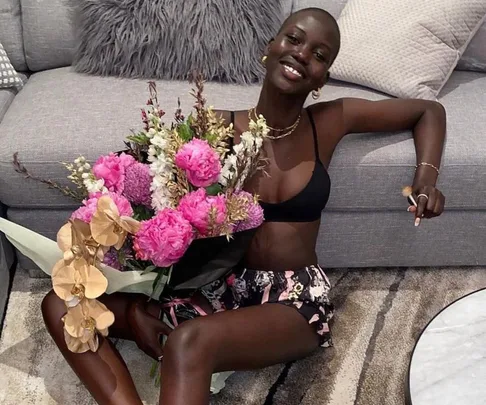 Smiling person on a sofa holding a vibrant bouquet of pink and white flowers.