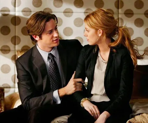 A man and woman sitting together on a couch, engaged in conversation, in a room with a polka dot wall pattern.