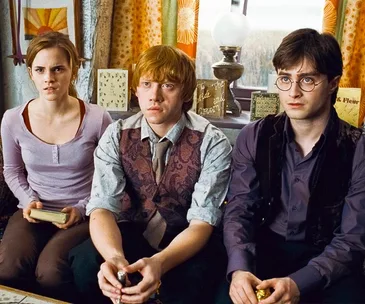 Three young characters from Harry Potter seated, looking intently forward indoors.