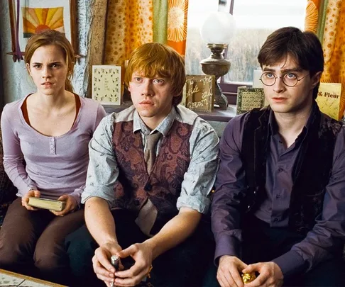 Three young characters from Harry Potter seated, looking intently forward indoors.