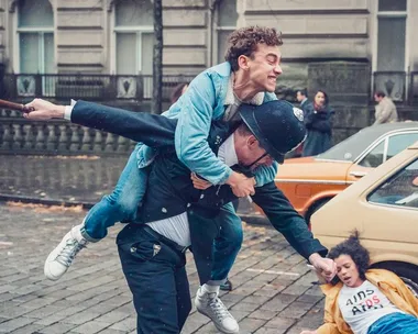 Protester piggybacks on a police officer during a street protest, with another protester falling nearby.