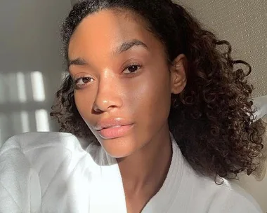 A woman with clear skin and curly hair in natural lighting.