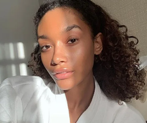 A woman with clear skin and curly hair in natural lighting.