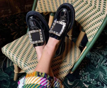 Black chunky loafers with jeweled buckles on a woven chair.