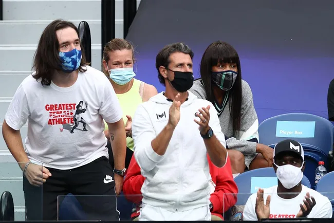 Crowd wearing masks cheering at a seated sports event, with focus on people clapping and showing enthusiasm.
