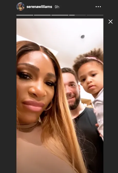 Family selfie with three people, a woman in front, a man in the middle, and a child with a headband in the background.