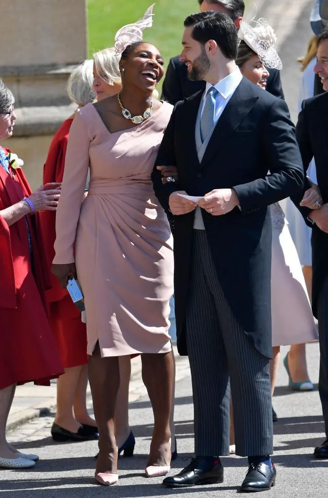 Couple in formal attire joyfully attending an outdoor event, surrounded by other attendees.