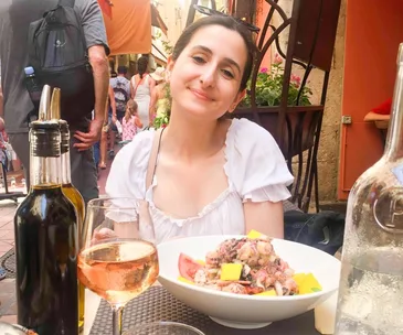 Woman smiling at an outdoor cafe table with food and drinks.