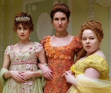 Three women in ornate Regency dresses and tiaras stand together in an elegant room.