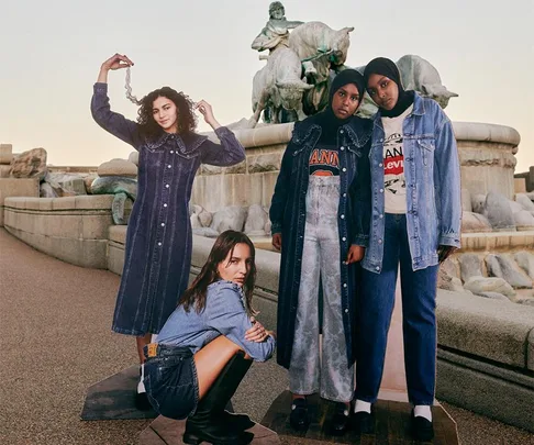 Four models in denim outfits pose in front of a stone fountain for the Levi's x Ganni collaboration.