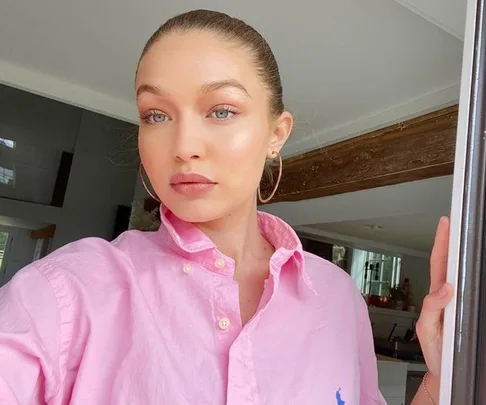 Person in a pink shirt with hoop earrings, standing in a bright room, looking at the camera.