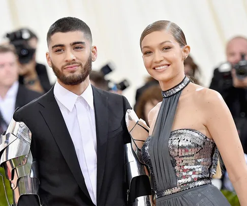 A couple poses on the red carpet, dressed in formal attire with metallic accents and smiling at the camera.