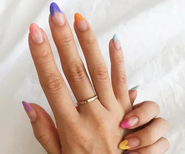 Colorful heart-tipped French manicure on a hand against a white background.