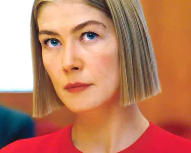 A woman with a short bob haircut and serious expression, wearing a red top, from the film "I Care a Lot."