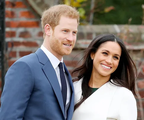 Prince Harry and Meghan Markle smiling outdoors wearing formal attire.