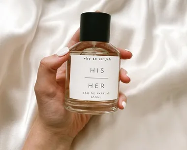 A hand holding a bottle of "Who is Elijah" His Her Eau de Parfum on a silky background.