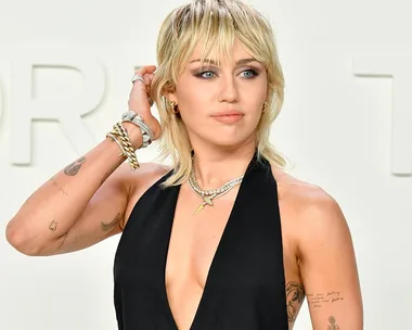 Woman with a blonde mullet hairstyle wearing a black halter top, accessorized with layered necklaces and bracelets.