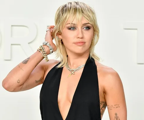 Woman with a blonde mullet hairstyle wearing a black halter top, accessorized with layered necklaces and bracelets.