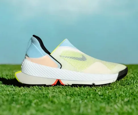 A side view of the Nike Go FlyEase shoe in pastel colors on grass, showcasing its foldable design.