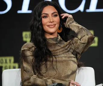 A woman with long dark hair wearing a striped outfit, smiling and seated during an event or interview.